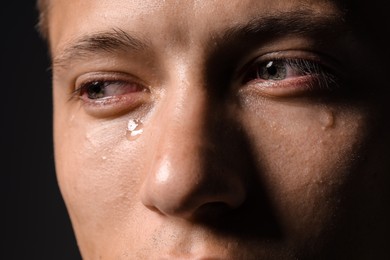 Photo of Sad man crying on black background, closeup