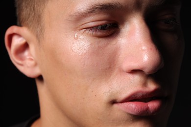 Photo of Sad man crying on black background, closeup