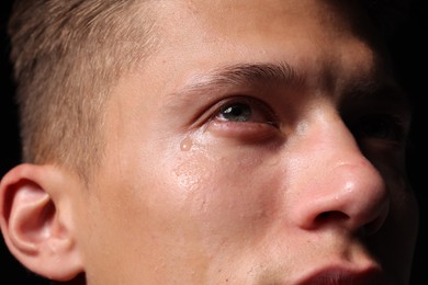 Photo of Sad man crying on black background, closeup