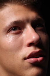 Photo of Sad man crying on black background, closeup