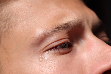 Photo of Sad man crying on black background, closeup