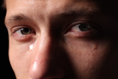 Photo of Sad man crying on black background, closeup
