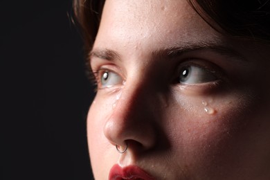 Photo of Sad woman crying on black background, closeup