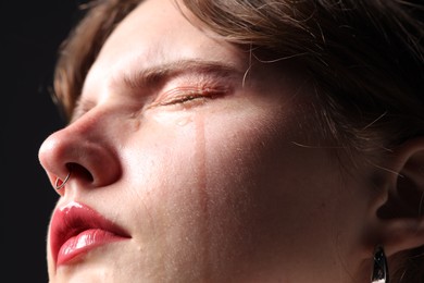 Photo of Sad woman crying on black background, closeup