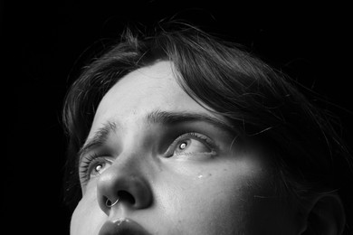 Photo of Sad woman crying on dark background, closeup. Black and white effect