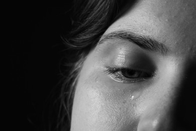 Photo of Sad woman crying on dark background, closeup. Black and white effect