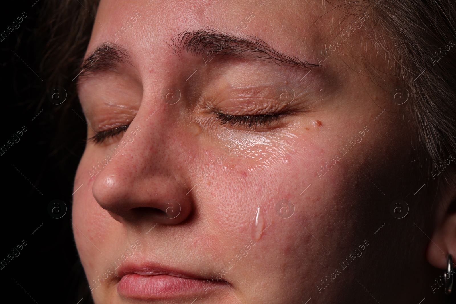 Photo of Sad woman crying on black background, closeup