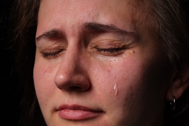 Photo of Sad woman crying on black background, closeup