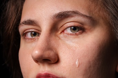 Photo of Sad woman crying on black background, closeup
