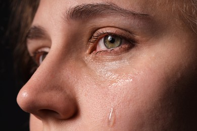 Photo of Sad woman crying on black background, closeup