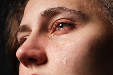 Photo of Sad woman crying on black background, closeup