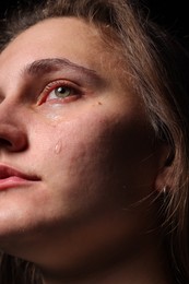 Photo of Sad woman crying on black background, closeup