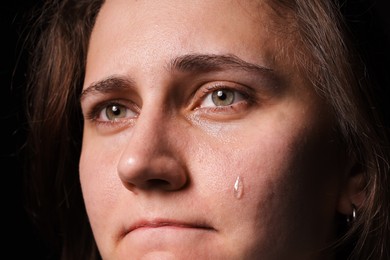 Photo of Sad woman crying on black background, closeup