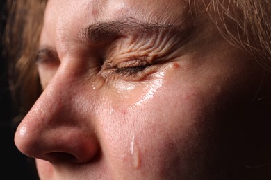 Photo of Sad woman crying on black background, closeup
