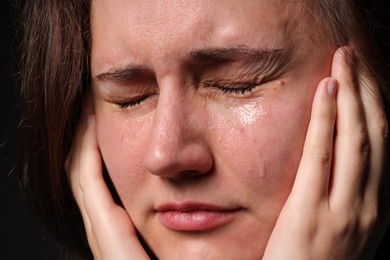 Photo of Sad woman crying on black background, closeup