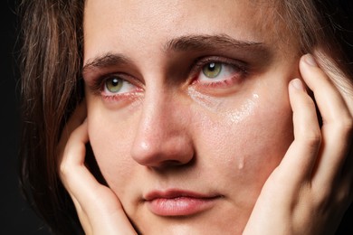 Photo of Sad woman crying on black background, closeup
