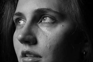 Photo of Sad woman crying on dark background, closeup. Black and white effect