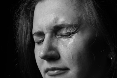 Photo of Sad woman crying on dark background, closeup. Black and white effect