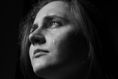 Photo of Sad woman crying on dark background, closeup. Black and white effect