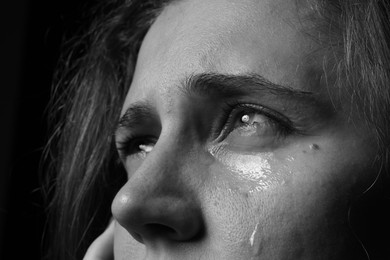 Photo of Sad woman crying on dark background, closeup. Black and white effect