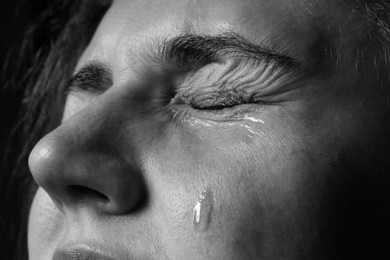 Photo of Sad woman crying on dark background, closeup. Black and white effect