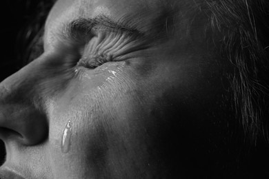 Photo of Sad woman crying on dark background, closeup. Black and white effect