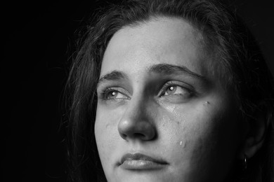 Photo of Sad woman crying on dark background, closeup. Black and white effect