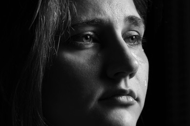 Photo of Sad woman crying on dark background, closeup. Black and white effect