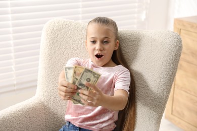 Photo of Little girl with pocket money in armchair at home