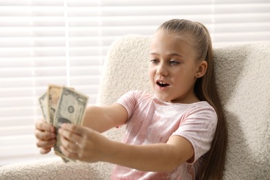 Photo of Little girl with pocket money in armchair at home