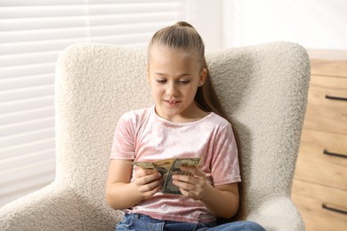 Photo of Little girl with pocket money in armchair at home