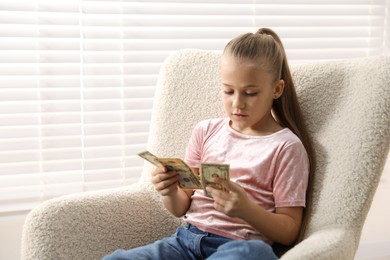 Photo of Little girl with pocket money in armchair at home
