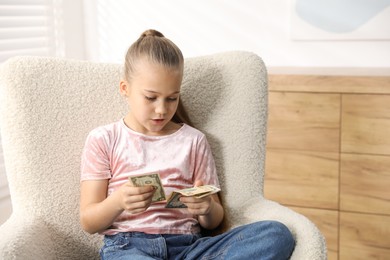 Photo of Little girl with pocket money in armchair at home