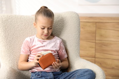 Photo of Little girl putting her pocket money into purse in armchair at home