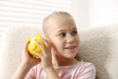 Photo of Pocket money. Little girl with piggy bank in armchair at home