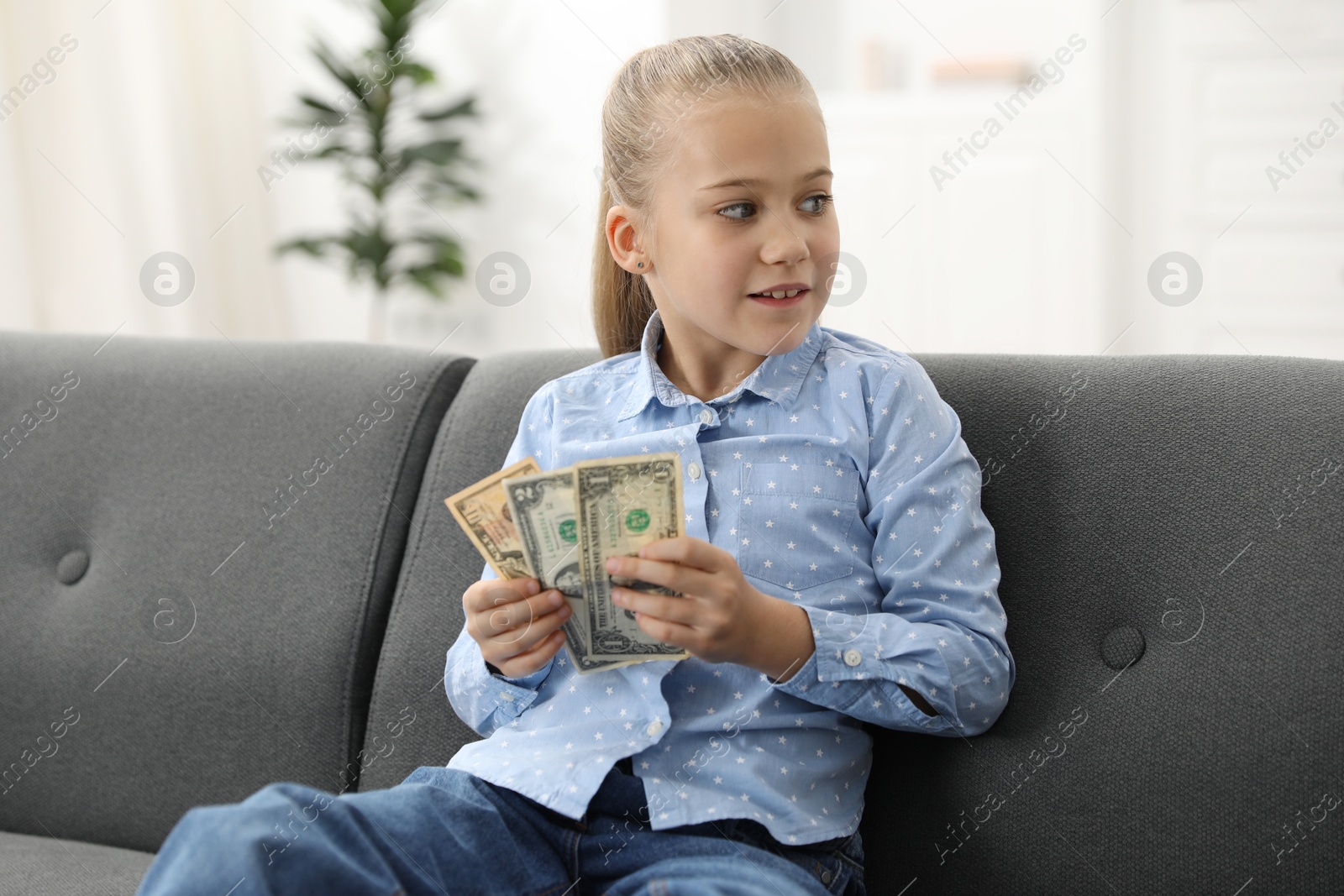 Photo of Little girl with pocket money on sofa at home