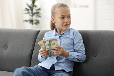 Photo of Little girl with pocket money on sofa at home