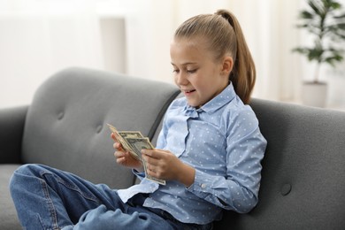 Photo of Little girl with pocket money on sofa at home