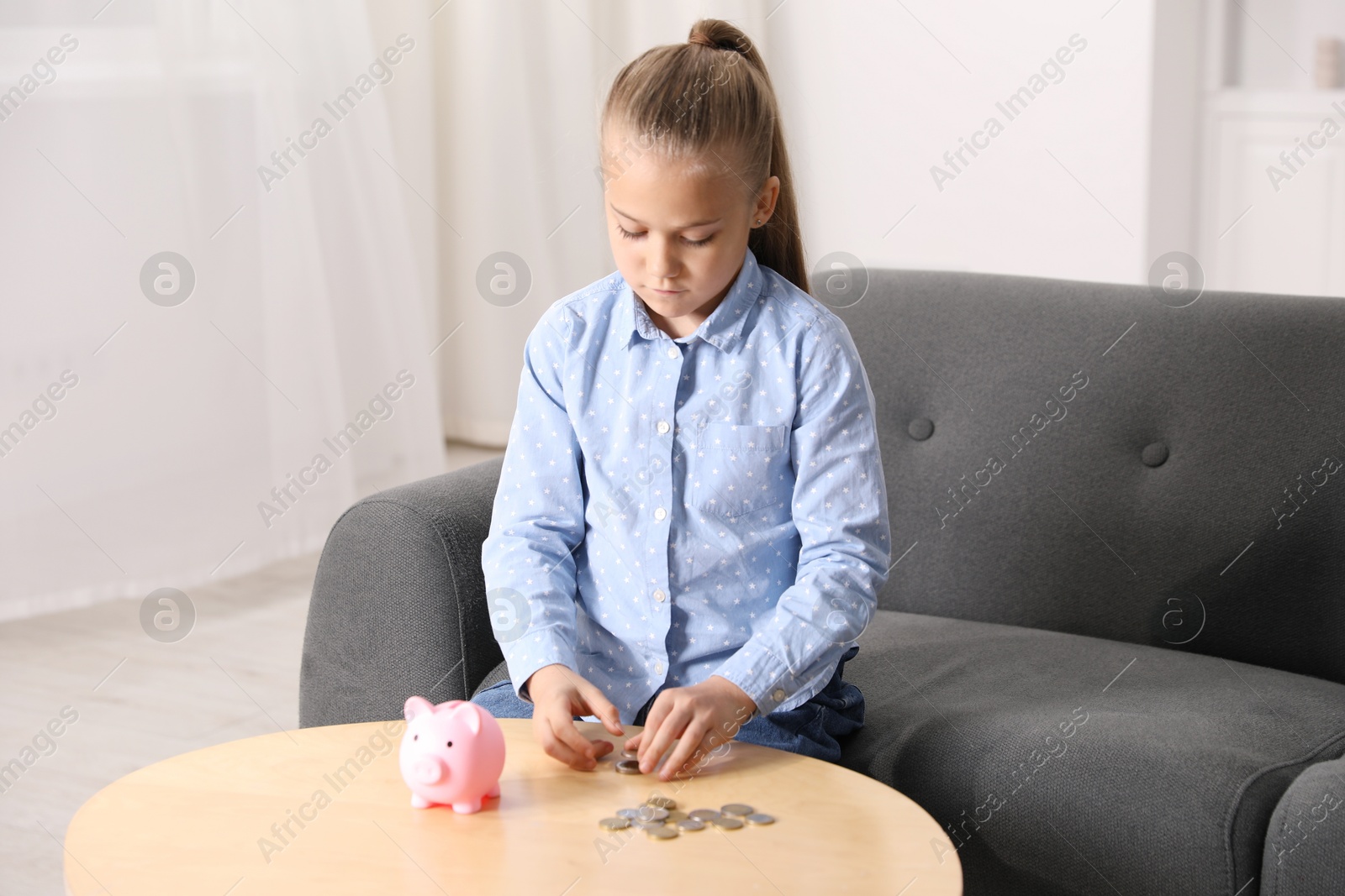 Photo of Little girl counting her pocket money at wooden table indoors