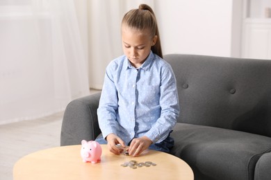 Photo of Little girl counting her pocket money at wooden table indoors