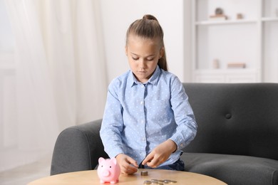 Photo of Little girl counting her pocket money at wooden table indoors