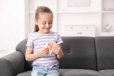 Photo of Little girl with pocket money on sofa at home, space for text