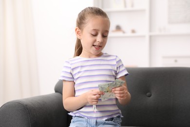 Photo of Little girl with pocket money on sofa at home