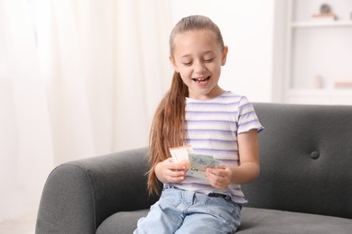 Photo of Little girl with pocket money on sofa at home