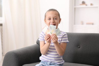 Photo of Little girl with pocket money on sofa at home