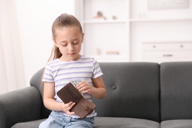 Photo of Little girl putting pocket money into purse on sofa at home, space for text