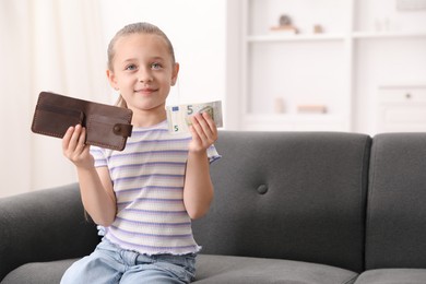 Photo of Little girl with pocket money and purse on sofa at home, space for text