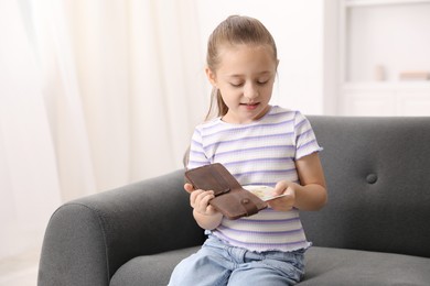 Photo of Little girl with pocket money on sofa at home