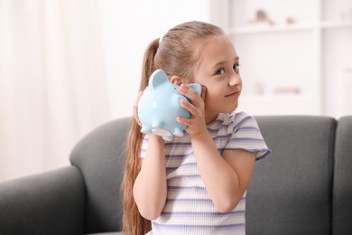 Photo of Pocket money. Little girl with piggy bank on sofa at home