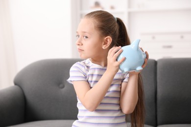 Photo of Pocket money. Little girl with piggy bank on sofa at home